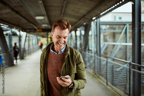 Obraz na płótnie Mature man using a smart phone while waiting for his train at the train station w salonie