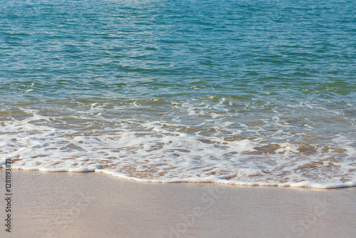 Blue sea water, waves and sand, with mountains on the background.