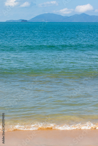 Blue sea water, waves and sand, with mountains on the background.