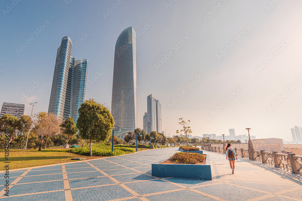 Young woman tourist with backpack walking and enjoying sunny day in modern city of Abu Dhabi, United Arab Emirates