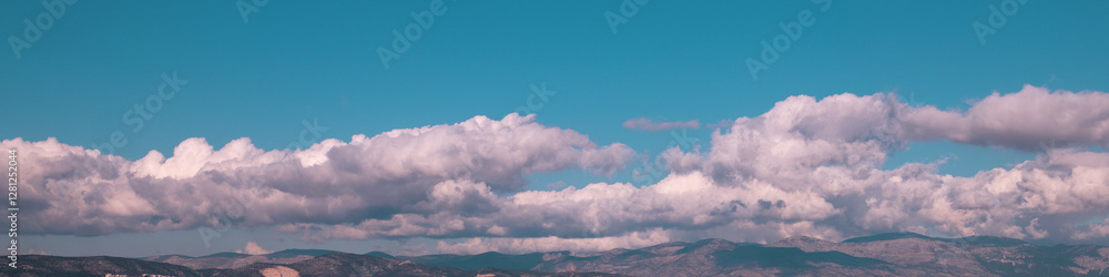 Obraz premium 4x1 banner is a band of white cumulus clouds hanging low over the rolling horizon of a blue sky
