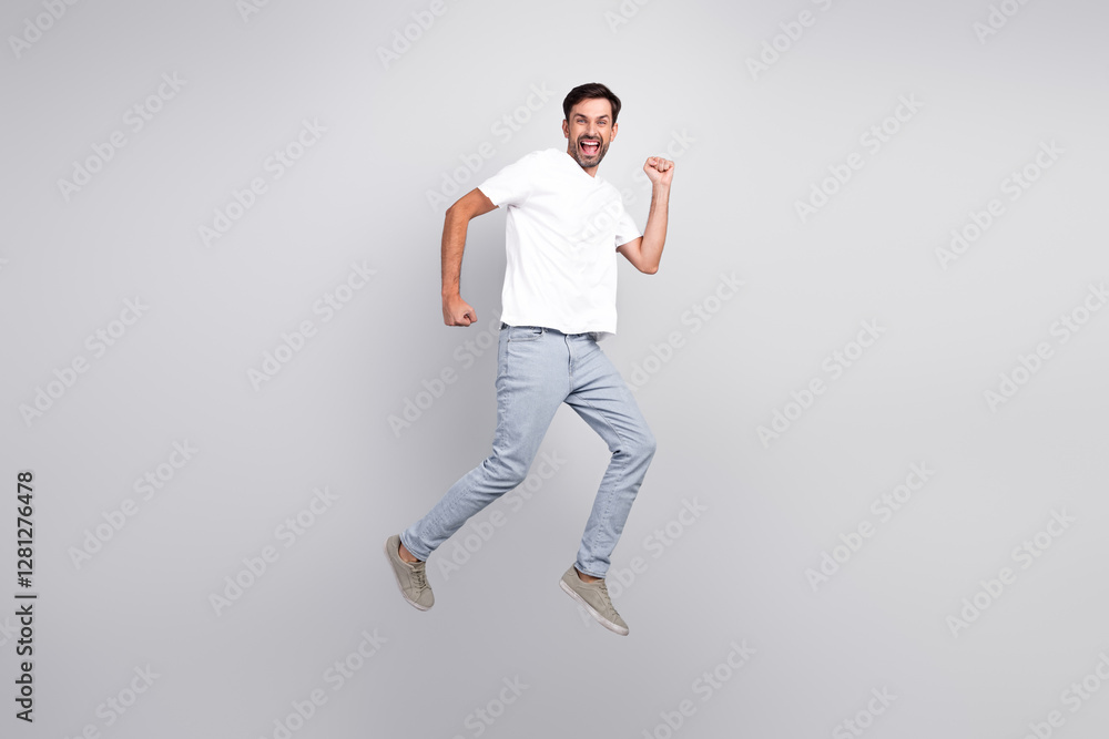 Excited young man jumping with a joyful pose in casual outfit against a grey background, expressing happiness and energy. Excited young man jumping with a joyful pose in casual outfit against a grey background, expressing happiness and energy.