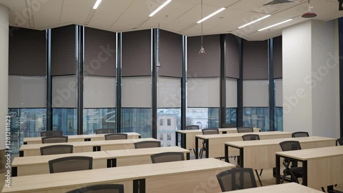 Modern empty classroom on high floor, lecture room, with panoramic windows and dark gray walls. Desks with chairs.
