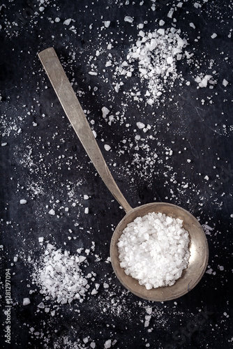 Top view of a spoon with coarse grained sea salt on black background. Flat lay. Top view. Food concept.