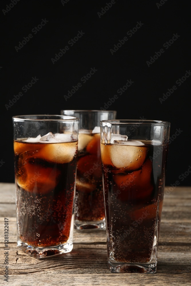 Refreshing cola with ice cubes in glasses on wooden table against black background, closeup Refreshing cola with ice cubes in glasses on wooden table against black background, closeup