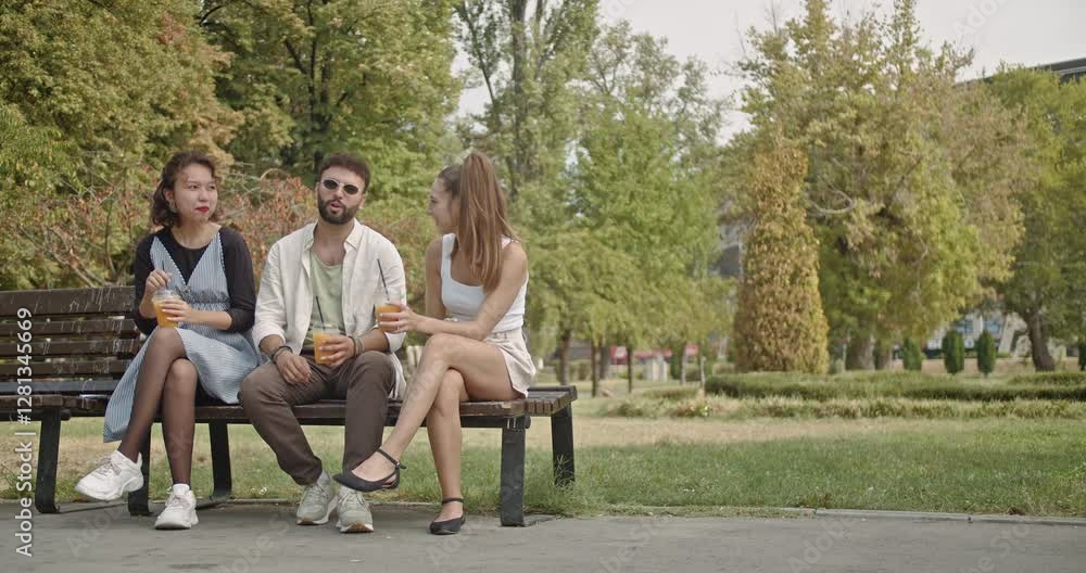 Three friends enjoy a summer day in the park, sitting on a bench, drinking juice, and chatting happily. Three friends enjoy a summer day in the park, sitting on a bench, drinking juice, and chatting happily.