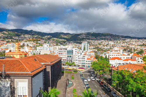 Obraz na płótnie Panoramic view of Funchal, Madeira, with terracotta roofed buildings, lush green hills and vibrant cityscape under partly cloudy sky. Mix of modern and traditional architecture highlights island charm w salonie