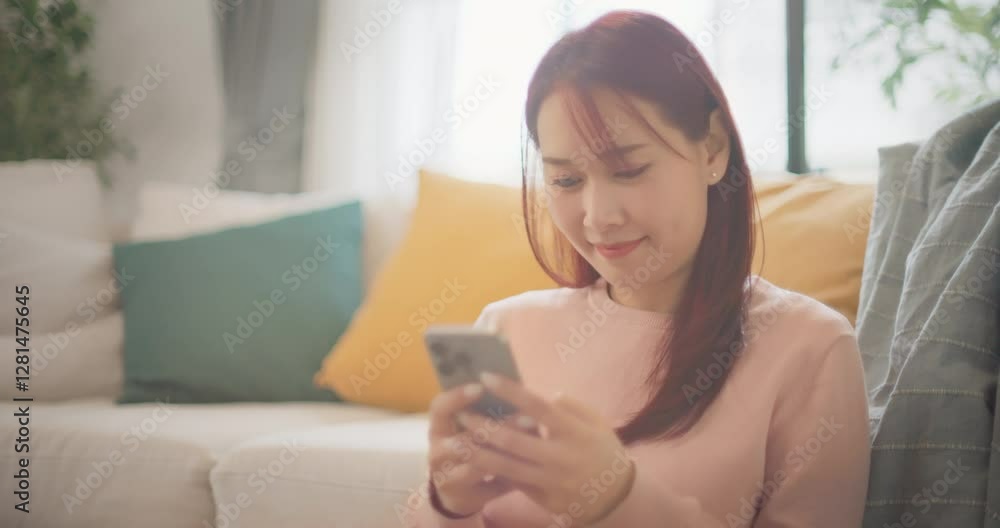 Smiling asian woman sitting in living room using cellphone texting, reading, sharing messages on social media. Relaxed female holding smartphone enjoy buying, ordering products online in apps at home. Smiling asian woman sitting in living room using cellphone texting, reading, sharing messages on social media. Relaxed female holding smartphone enjoy buying, ordering products online in apps at home.