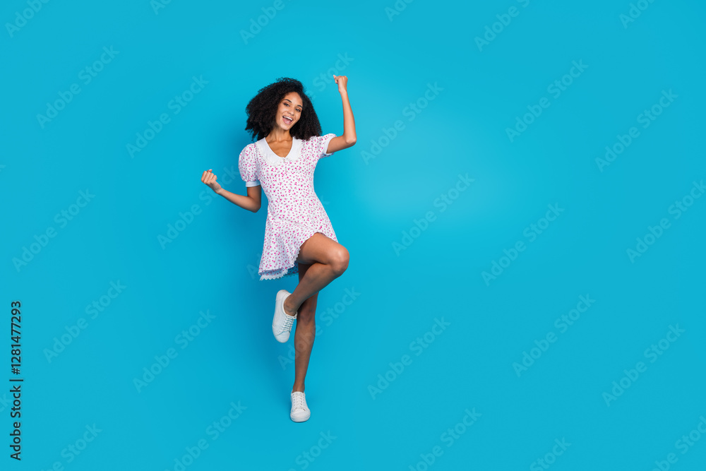 Obraz premium Smiling young woman in a floral dress posing against vibrant blue background expressing joyful and stylish summer vibes