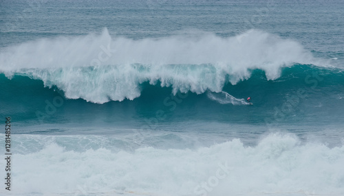 Lonely surfer on Huge Atlantic ocean wave during international surfers challenge at Praia do Norte in Nazare, Farol da Nazaré, Portugal where Guinness World Record for the highest surfing was set