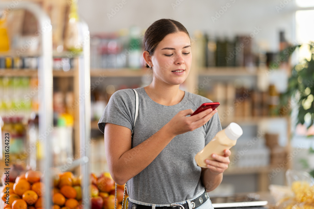Fototapeta premium Young woman buyer scanning qr code for mayonnaise sauce in grocery store