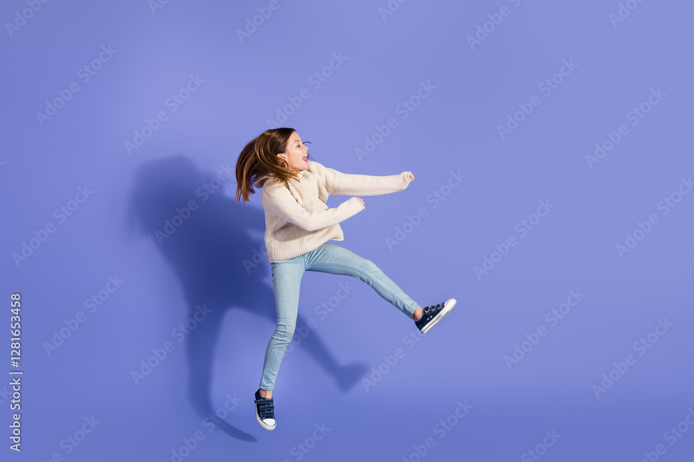 Happy young girl jumping in casual outfit against a purple background Happy young girl jumping in casual outfit against a purple background