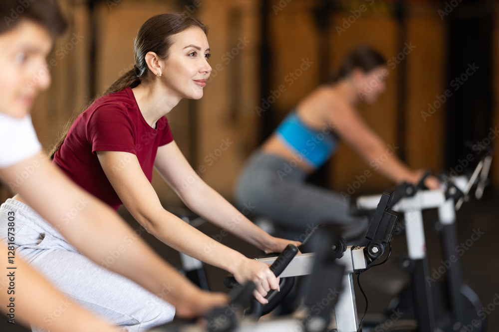 Girl hardly performs exercises on exercise bicycle during fitness class. Gym and fitness equipment, visitors are engaged in physical exercises during training Girl hardly performs exercises on exercise bicycle during fitness class. Gym and fitness equipment, visitors are engaged in physical exercises during training