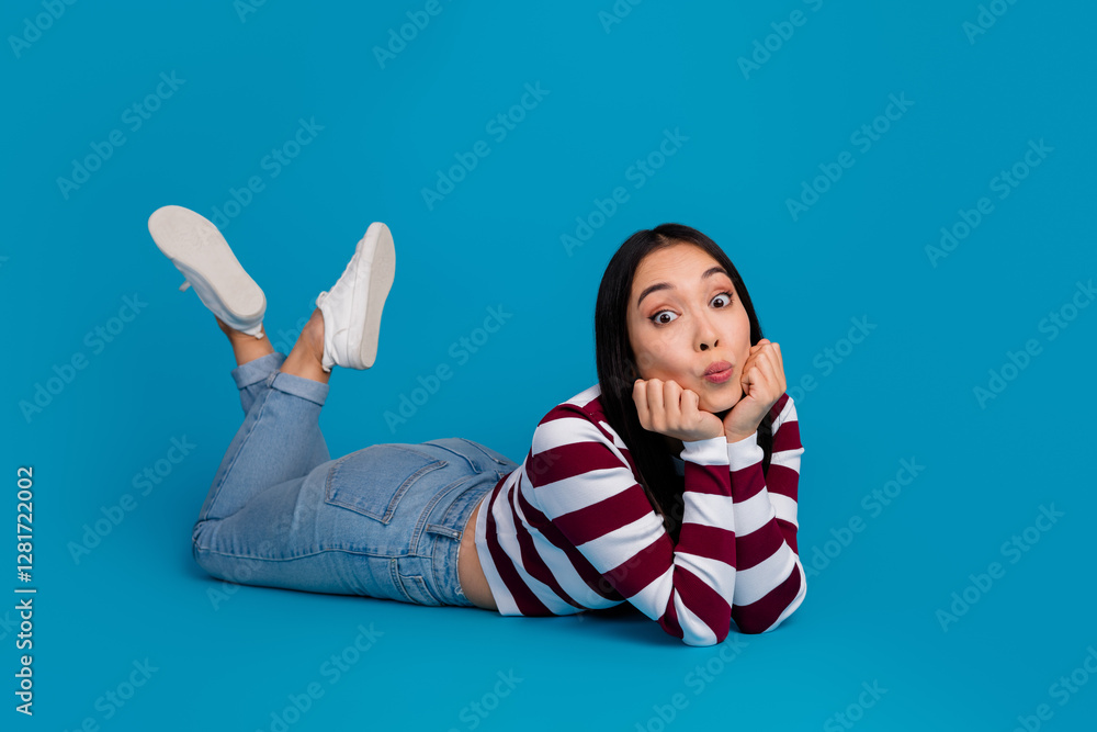 Smiling young woman posing playfully on a blue background in trendy casual style, expressing joy Smiling young woman posing playfully on a blue background in trendy casual style, expressing joy