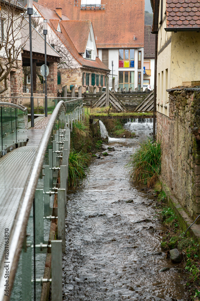 Urban Stream Walkway. A narrow, winding stream flows between a modern glass-railed walkway and the walls of an urban building. The combination of natural and man-made elements creates a unique contras Urban Stream Walkway. A narrow, winding stream flows between a modern glass-railed walkway and the walls of an urban building. The combination of natural and man-made elements creates a unique contras