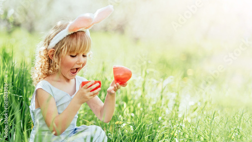 Easter egg hunt. Girl child Wearing Bunny Ears Running To Pick Up Egg In Garden. Easter tradition. Baby with basket full of colorful eggs.