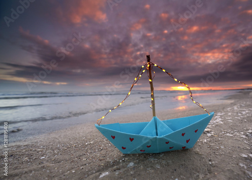 Fototapeta Naklejka Na Ścianę i Meble -  lovely romantic lantern blue paper boat with red hearts and light string on the frozen winter beach