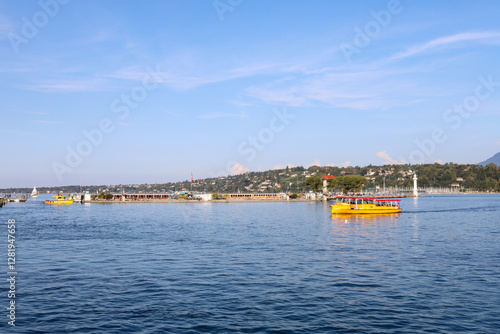 Scenic view of a yellow water taxi boat on Lake Geneva in Switzerland under a bright blue sky with the city coastline in the background.