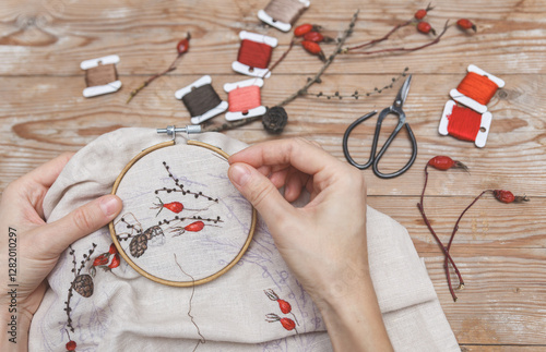 Woman is embroidering larch branches and hawthorn berries with a needle. Handmade embroidery process.