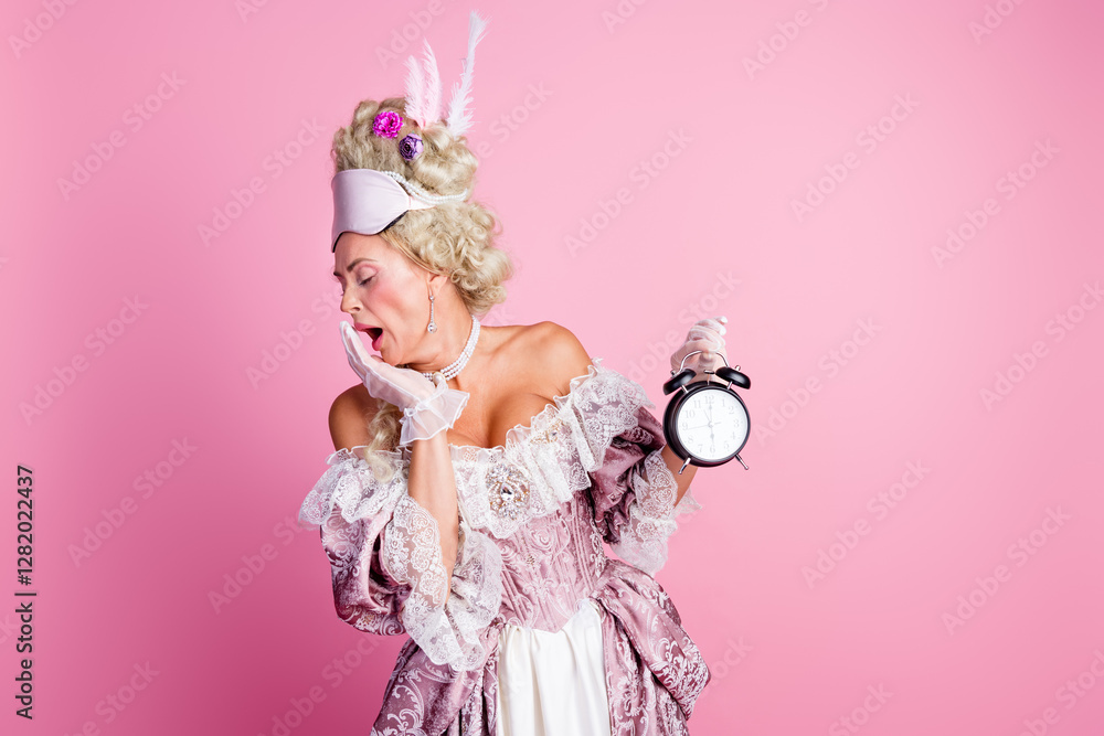 Fototapeta premium Elegant woman dressed in baroque costume yawning with vintage clock in hand against pink background