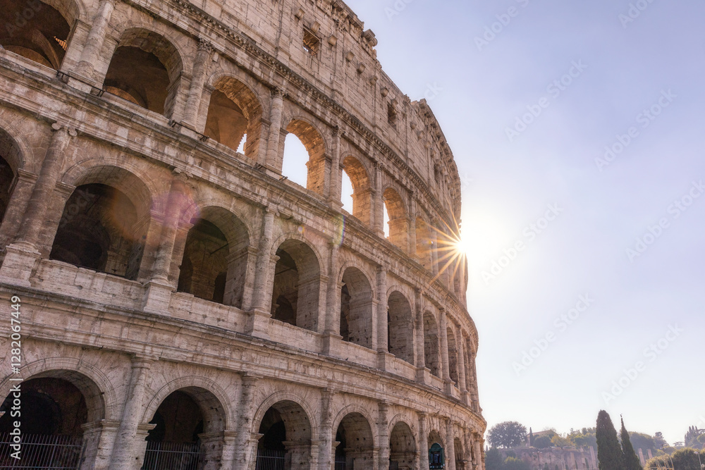 Fototapeta premium Roman Colosseum at sunset with sun rays coming through the structure. Rome, Italy