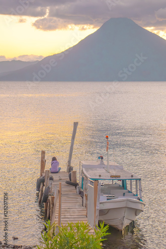 Hermosa fotografía de un chica sentada frente al lago de Atitlán en Guatemala al atardecer con los volcanes de San Pedro y Tolimán de fondo. photo