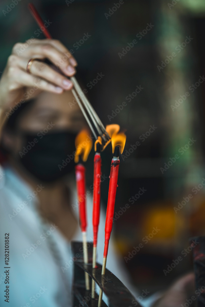 Naklejka premium Hand Lighting Red Incense Sticks in a Temple Ritual, Close-Up of Spiritual Practice at a shrine