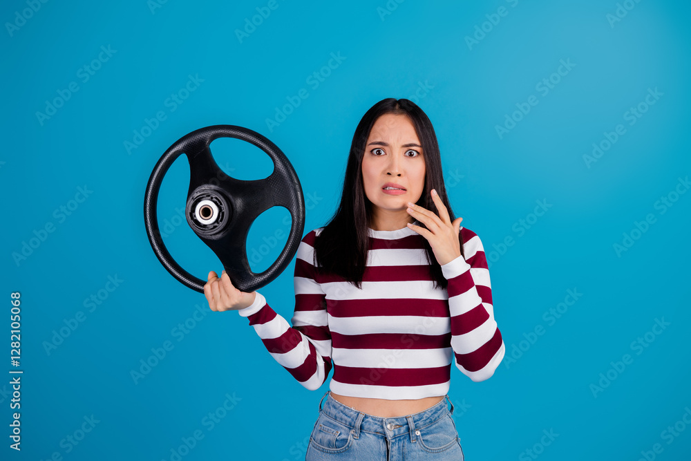 Surprised Young Woman Holding a Steering Wheel Against a Blue Background Surprised Young Woman Holding a Steering Wheel Against a Blue Background
