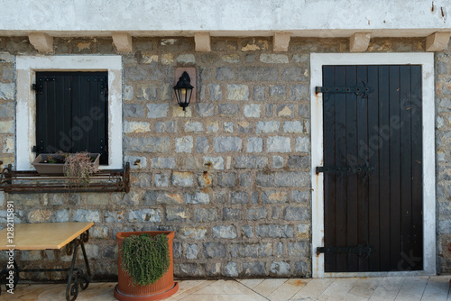 Rustic Mediterranean stone wall with a black wooden door and shuttered window in a medieval Venetian fort