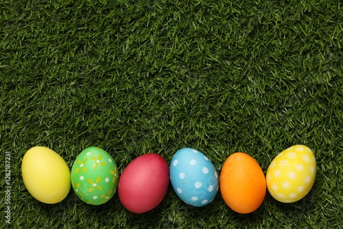 Beautiful decorated Easter eggs on green grass, flat lay. Space for text