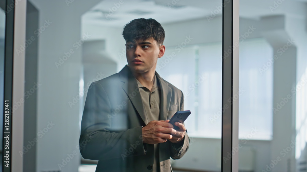 Puzzled businessman thinking decision holding cellphone at glass hall closeup Puzzled businessman thinking decision holding cellphone at glass hall closeup