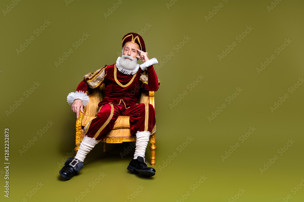 A Senior Man in Renaissance Noble Costume Sitting on a Golden Chair Against Khaki Background A Senior Man in Renaissance Noble Costume Sitting on a Golden Chair Against Khaki Background