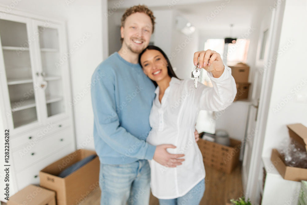 Happy European expecting spouses showing key from their own apartment, celebrating moving to own house, selective focus on key Happy European expecting spouses showing key from their own apartment, celebrating moving to own house, selective focus on key