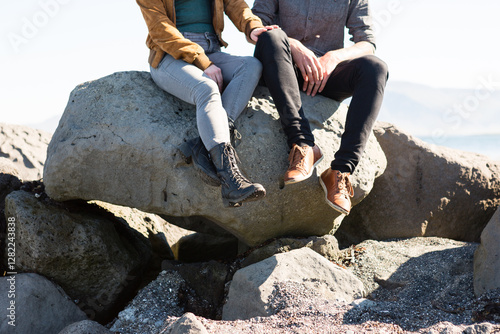 Couple sitting on large coastal rocks wearing casual outdoor attire.