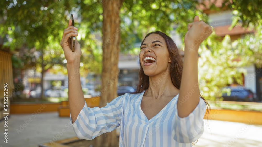 Woman celebrating outdoors in an urban park, holding a phone and smiling in a city setting under a tree in bright sunlight Woman celebrating outdoors in an urban park, holding a phone and smiling in a city setting under a tree in bright sunlight