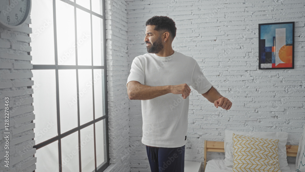 Obraz premium Young man stretches in a bedroom with sunlight streaming through a large window, surrounded by white brick walls and stylish decor