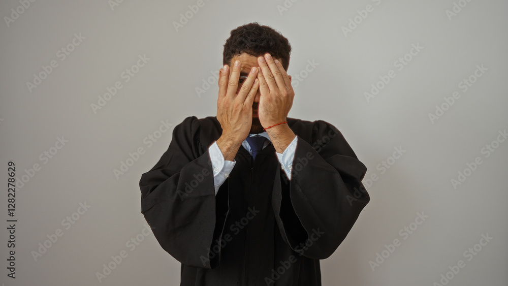 Young man in judicial robes hiding face with hands isolated against white background Young man in judicial robes hiding face with hands isolated against white background