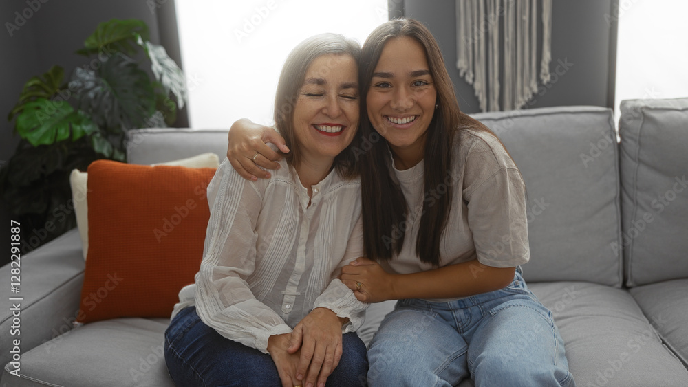 Mother and daughter smiling and hugging on a couch in the living room, portraying family love and bonding indoors. Mother and daughter smiling and hugging on a couch in the living room, portraying family love and bonding indoors.