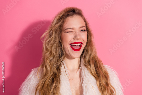 Charming young woman winking and smiling with bright red lips, wearing fur coat against vibrant pink background, showcasing style and joy photo