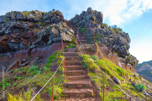 Obraz na płótnie Stone steps leading up a rocky hill, with railing on both sides for support. Steps are surrounded by green vegetation, and the sky is partly cloudy, creating a scenic and inviting path for hikers w salonie