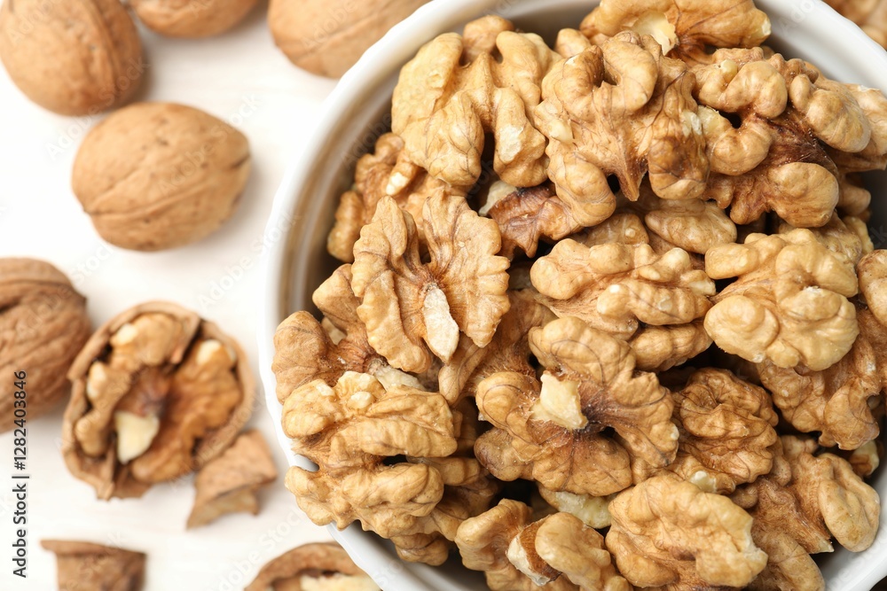 Peeled walnuts in bowl and whole ones on light table, flat lay Peeled walnuts in bowl and whole ones on light table, flat lay