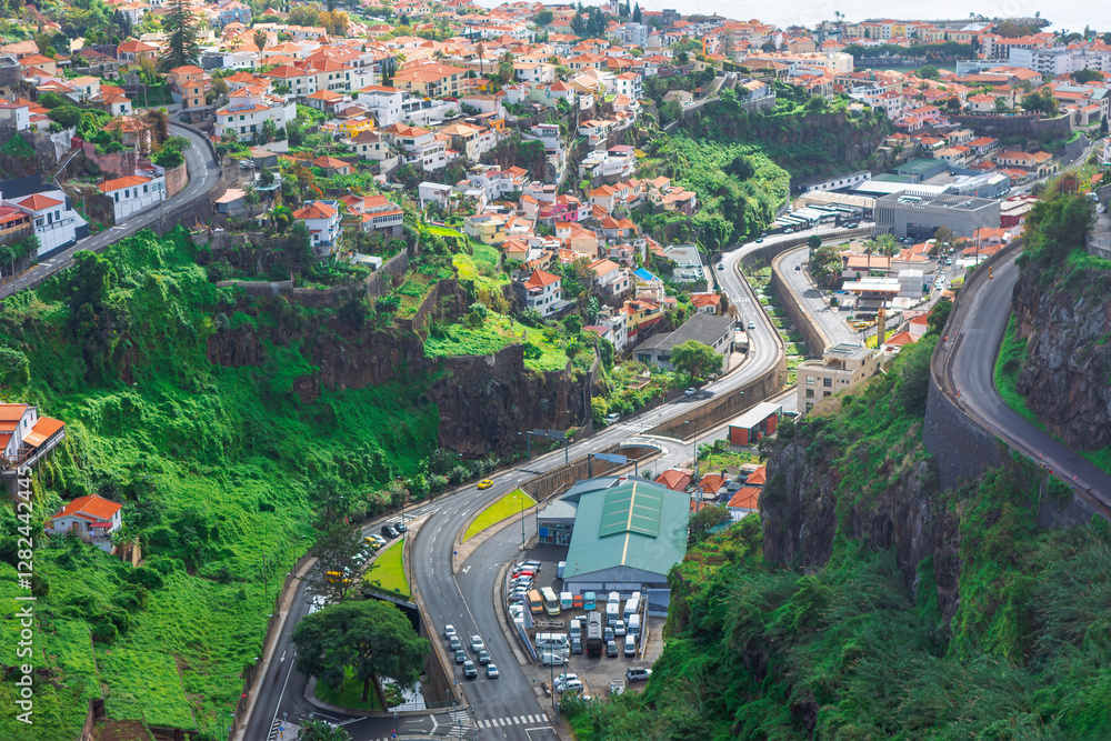 Stunning aerial view of Funchal, Madeira, showcasing winding roads, terraced houses with red roofs and green cliffs. Mix of urban development and natural landscapes highlights city unique topography