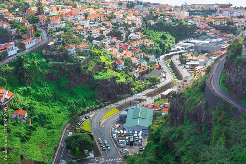 Obraz na płótnie Stunning aerial view of Funchal, Madeira, showcasing winding roads, terraced houses with red roofs and green cliffs. Mix of urban development and natural landscapes highlights city unique topography w salonie