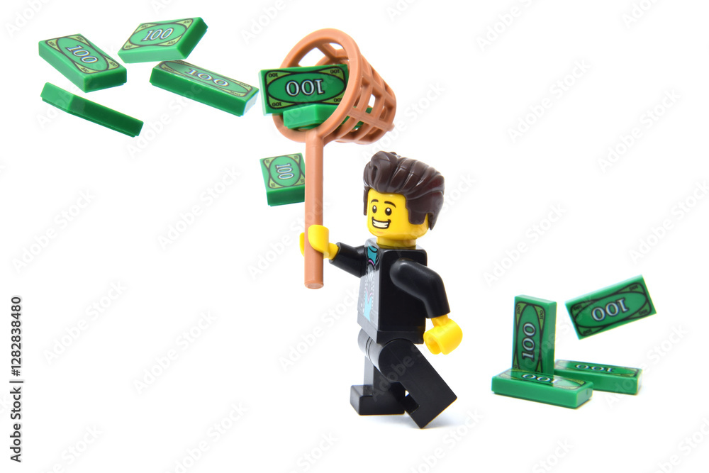 Naklejka premium Lego minifigure of happy male is counting his money green banknotes isolated on white. Editorial illustrative image of finance and banking