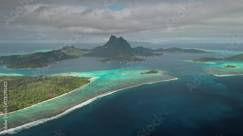 Stunning aerial view of Bora Bora island showing the turquoise lagoon, reef barrier, and lush greenery under a cloudy sky in French Polynesia. Travel tropical vacation concept. Natural background