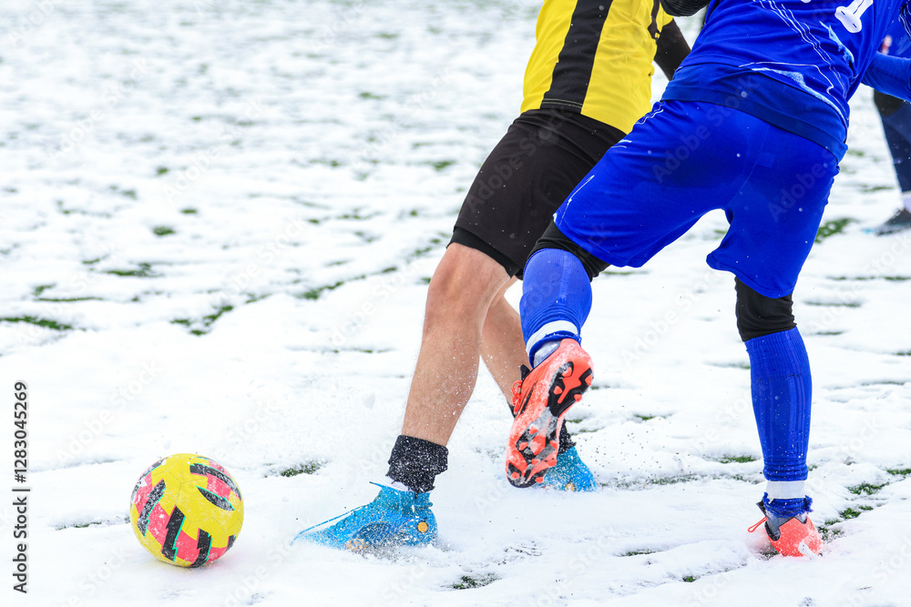 Two young football soccer players in a competitive match on a snow-covered field, showcasing intensity and athleticism in winter conditions.