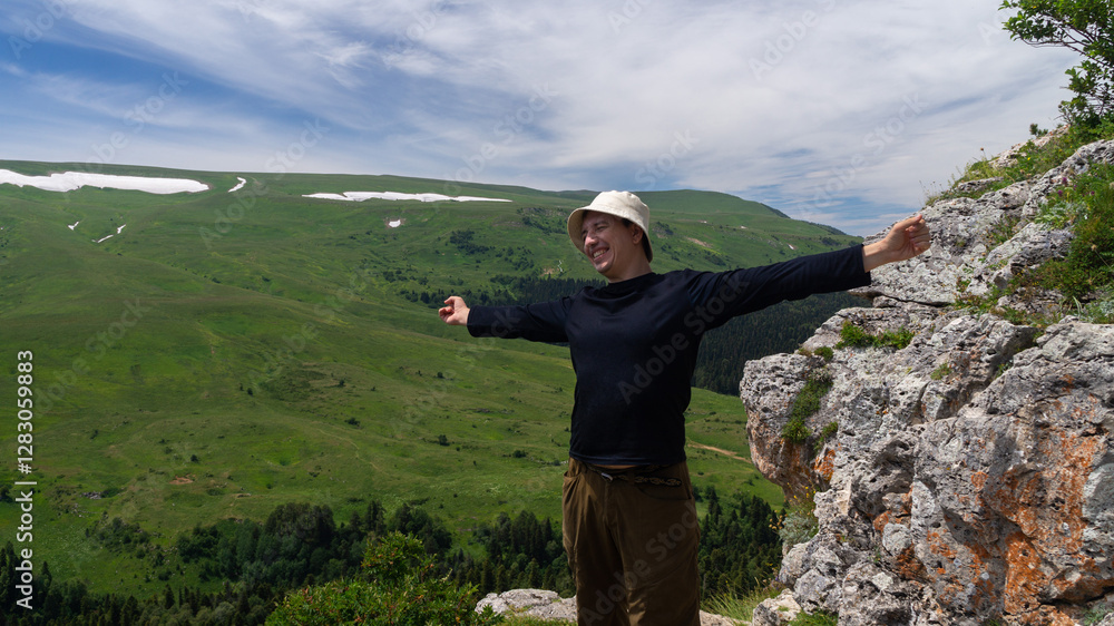 Obraz premium Young man stretching happily on top of mountain in summer against green plateau background