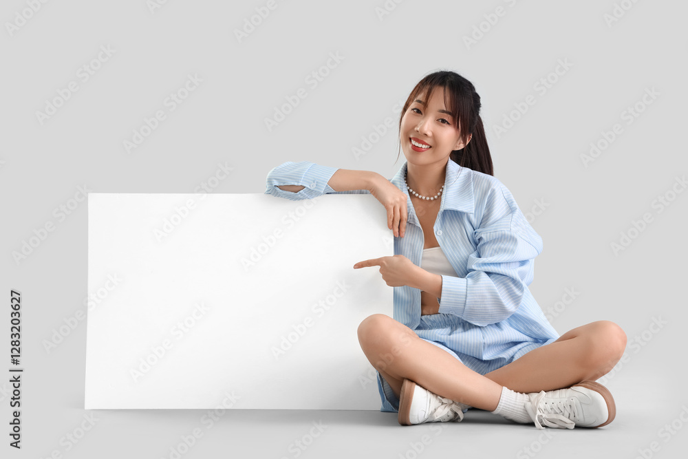 Young Asian woman with blank poster sitting on light background Young Asian woman with blank poster sitting on light background