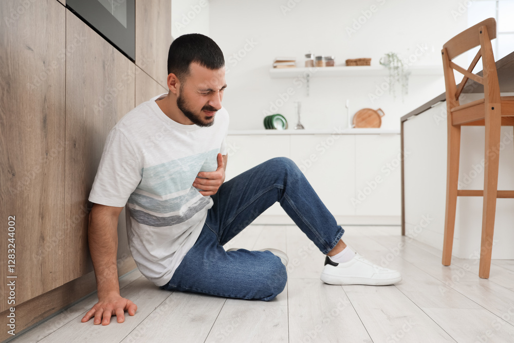 Young man suffering from chest pain on floor in kitchen Young man suffering from chest pain on floor in kitchen