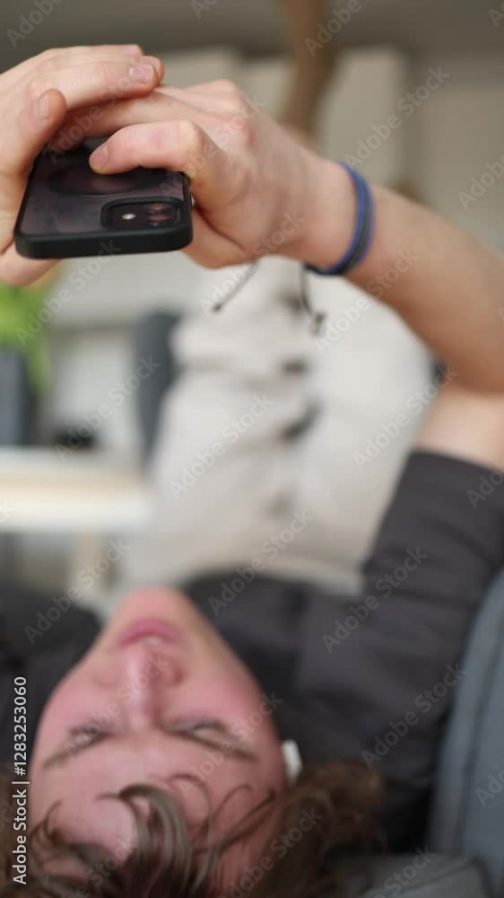Vertical screen: The man is holding his phone up with both hands while lying down. This posture, with constant phone use, could lead to the negative effects of phone radiation. Vertical screen: The man is holding his phone up with both hands while lying down. This posture, with constant phone use, could lead to the negative effects of phone radiation.